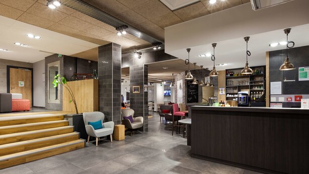 Un moderno vestíbulo de hotel con un mostrador de recepción, una zona de estar y una escalera que conduce a otro nivel.