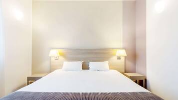 A hotel room with a large bed, two bedside lamps, and a wooden headboard.