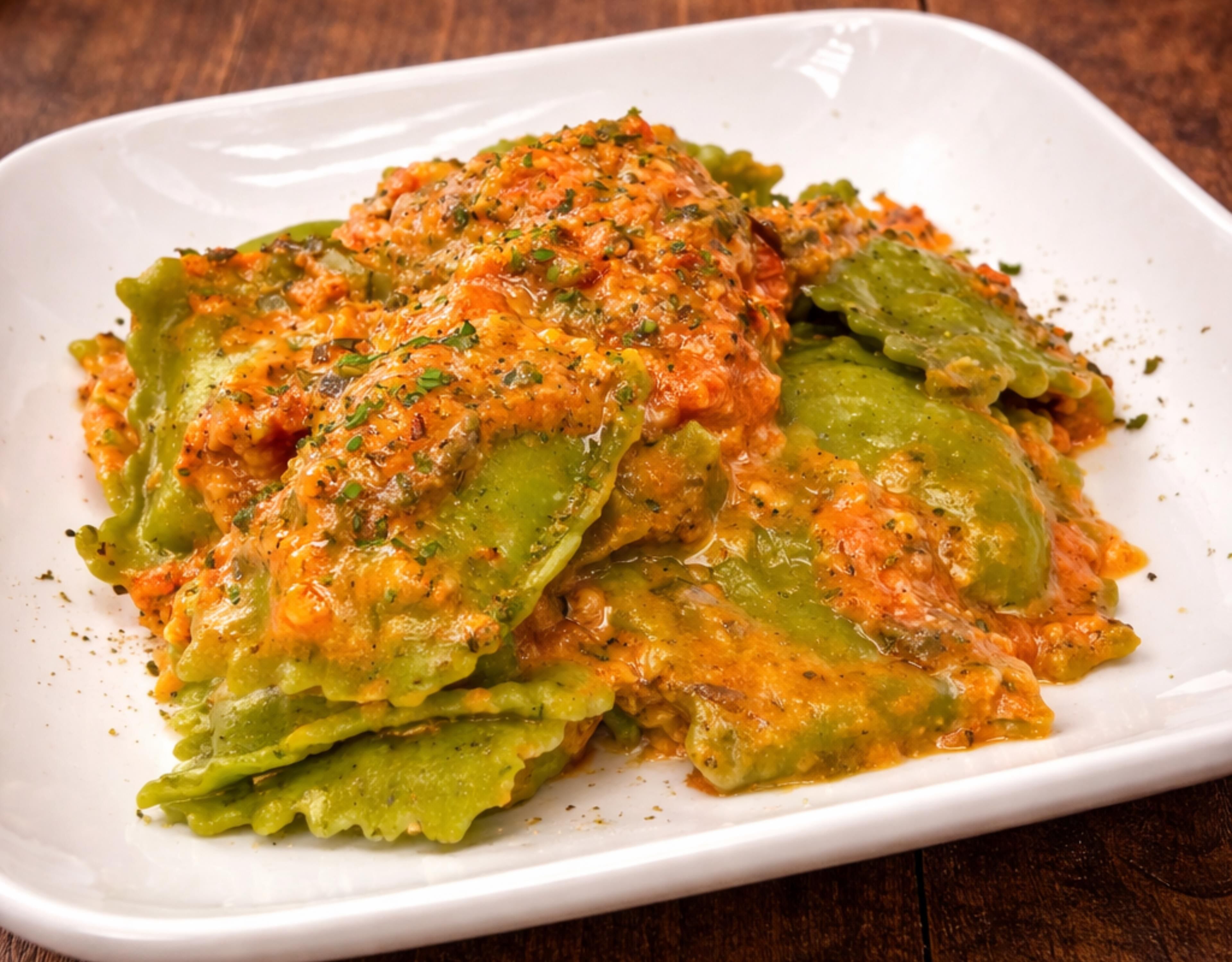 A white rectangular plate with a dish of stuffed vegetables, possibly zucchini, topped with a tomato-based sauce and herbs.