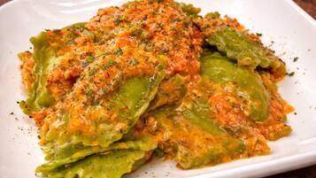 Plato blanco rectangular con guiso de verduras, posiblemente calabacín, cubierto con salsa de tomate y hierbas.