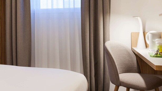 A hotel room with a bed, a desk, a chair, a lamp, and a window with curtains. - Hotel Campanile Metz Nord - Talange (Talange)