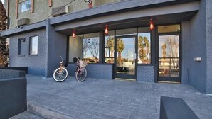 Een gebouw met een modern ontwerp, met een grote glazen ingang, een fiets voor de deur en een trap die naar de ingang leidt.
