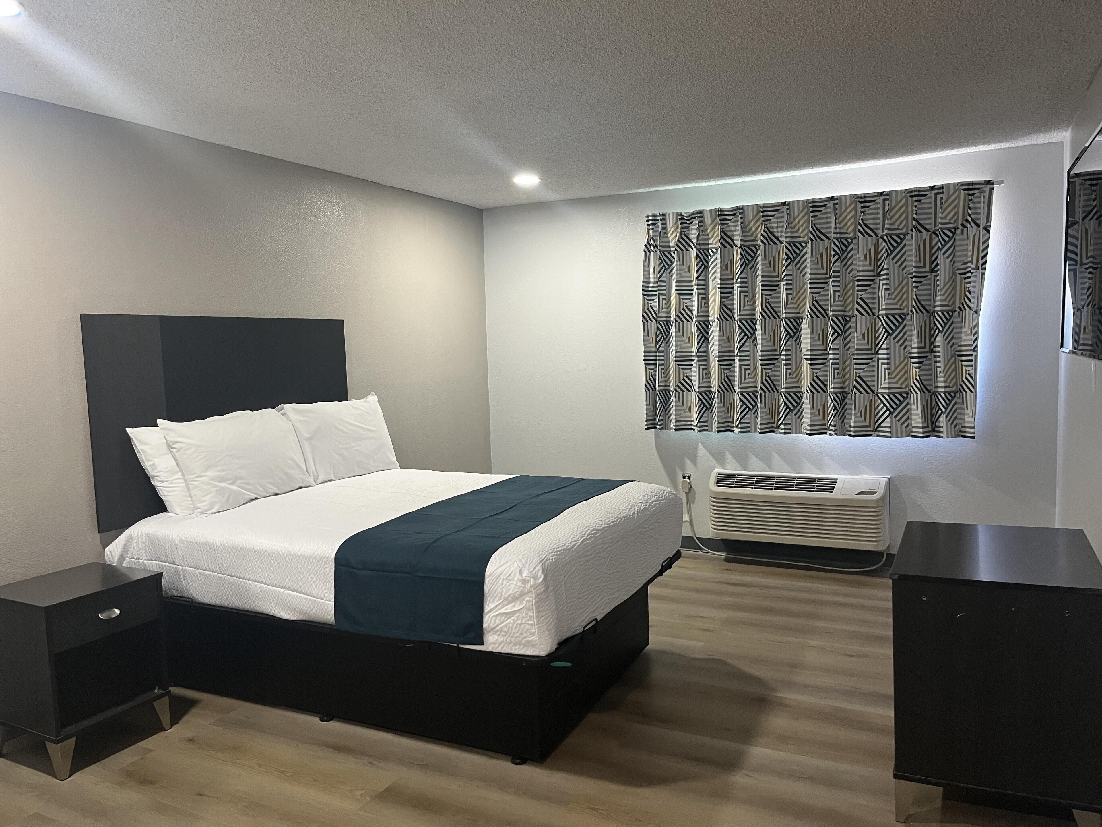 A modern bedroom with a bed, bedside tables, a heater, and patterned curtains.
