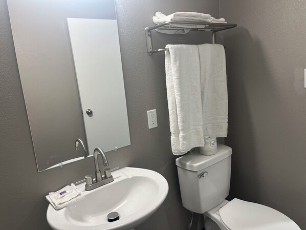 A bathroom with a white sink, a mirror, a towel rack with folded towels, and a toilet. - Motel 6 - Las Vegas, NV – Downtown Fremont St Experience (Las Vegas)