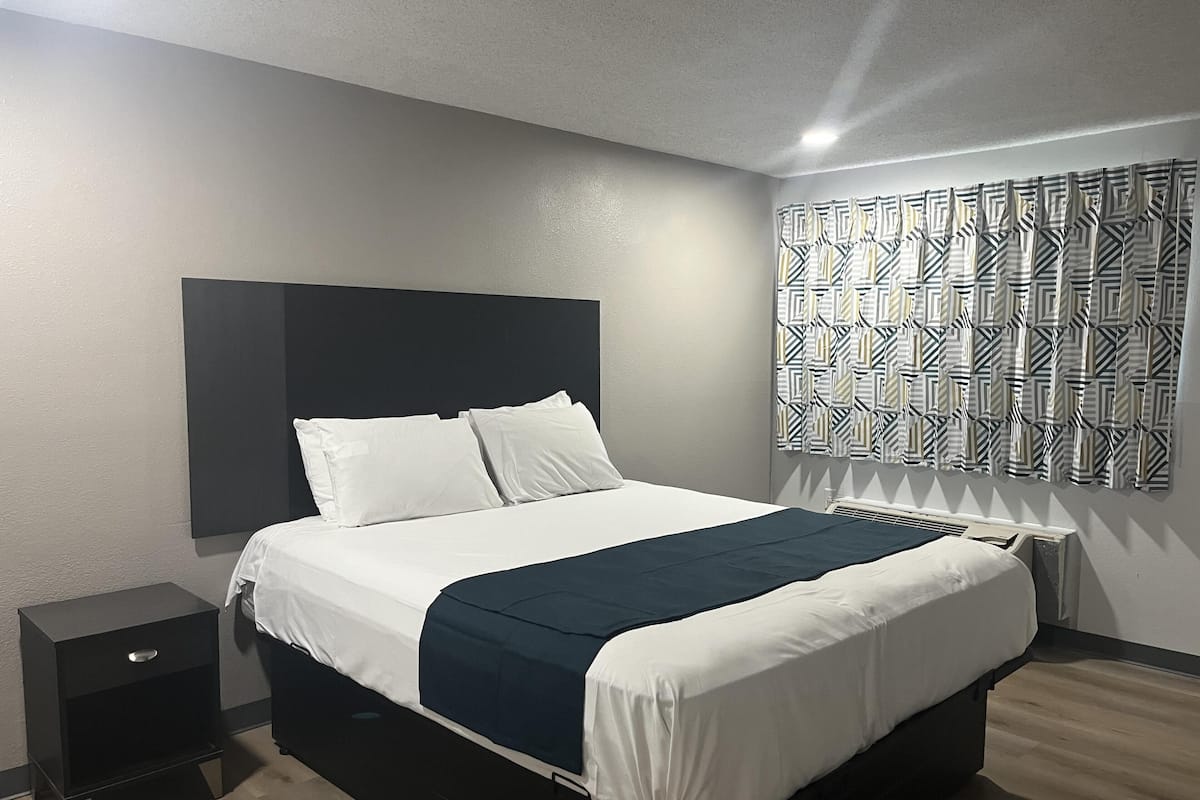A modern bedroom with a bed, a nightstand, a patterned curtain, and a radiator.