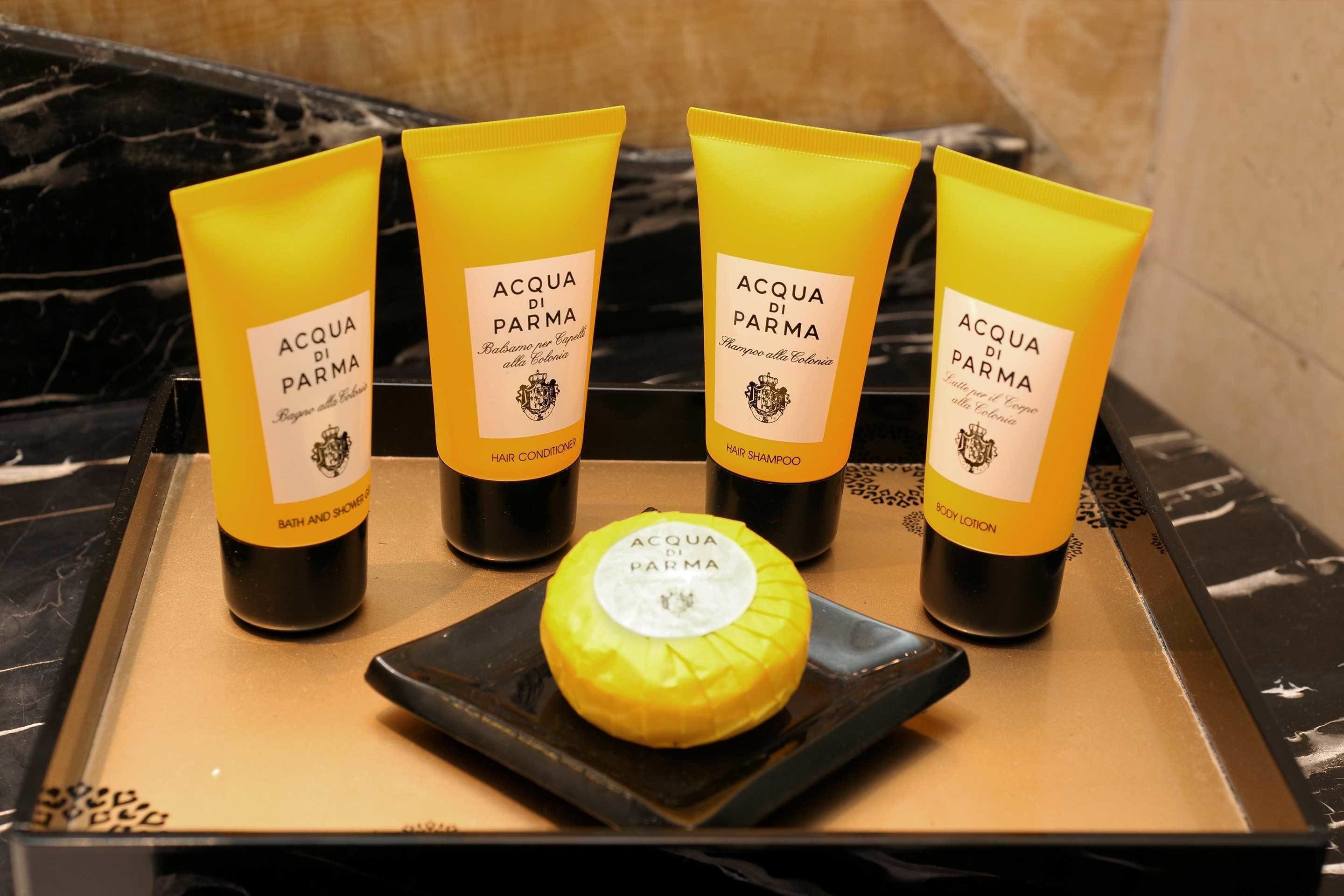 Four yellow bottles of Acqua di Parma hair products and a body lotion on a black tray.