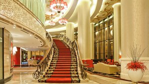 A grand staircase with ornate railings and red carpet, leading to a seating area with a large vase of red flowers. - The Trans Luxury Hotel (Bandung)