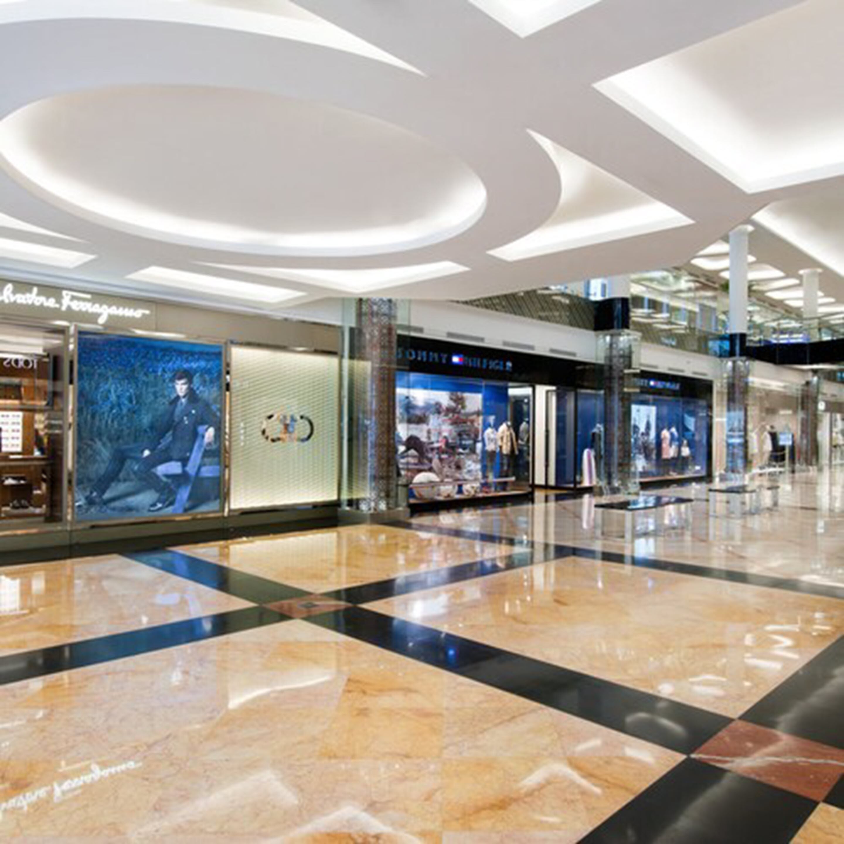 Un centro comercial amplio con suelo de mármol pulido, tiendas de lujo como Ferragamo y Tommy Hilfiger, y un diseño de techo moderno.