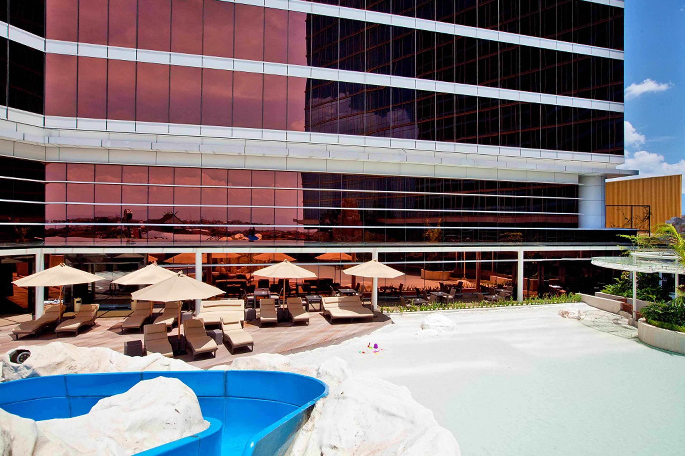 A modern hotel with a pool area featuring lounge chairs and umbrellas.