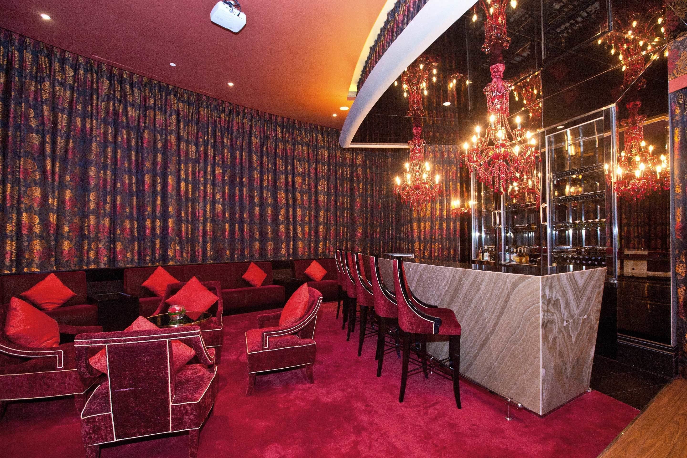 A bar area with red upholstered seating, a marble bar counter, and a chandelier.