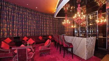 A bar area with red upholstered seating, a marble bar counter, and a chandelier.