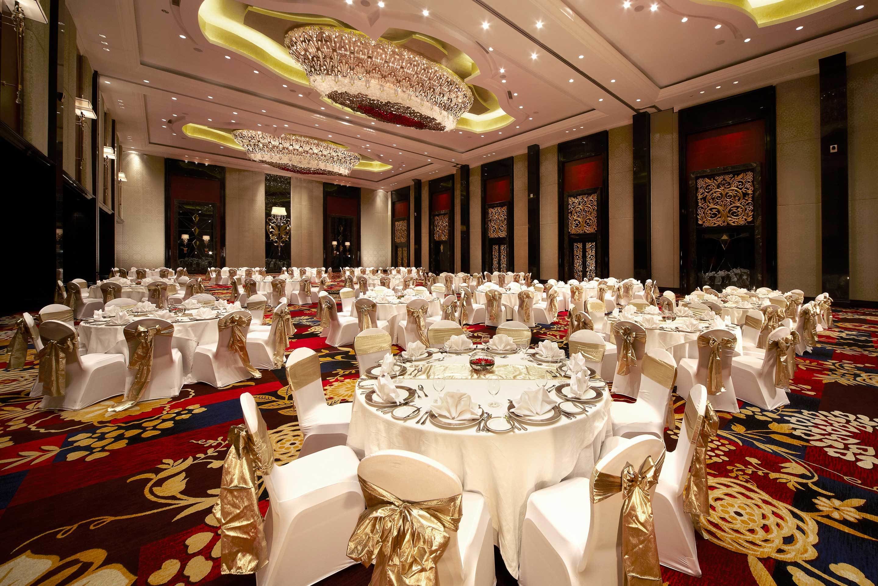 Un salón de banquetes con mesas redondas dispuestas para un evento formal, con cintas doradas y manteles blancos.