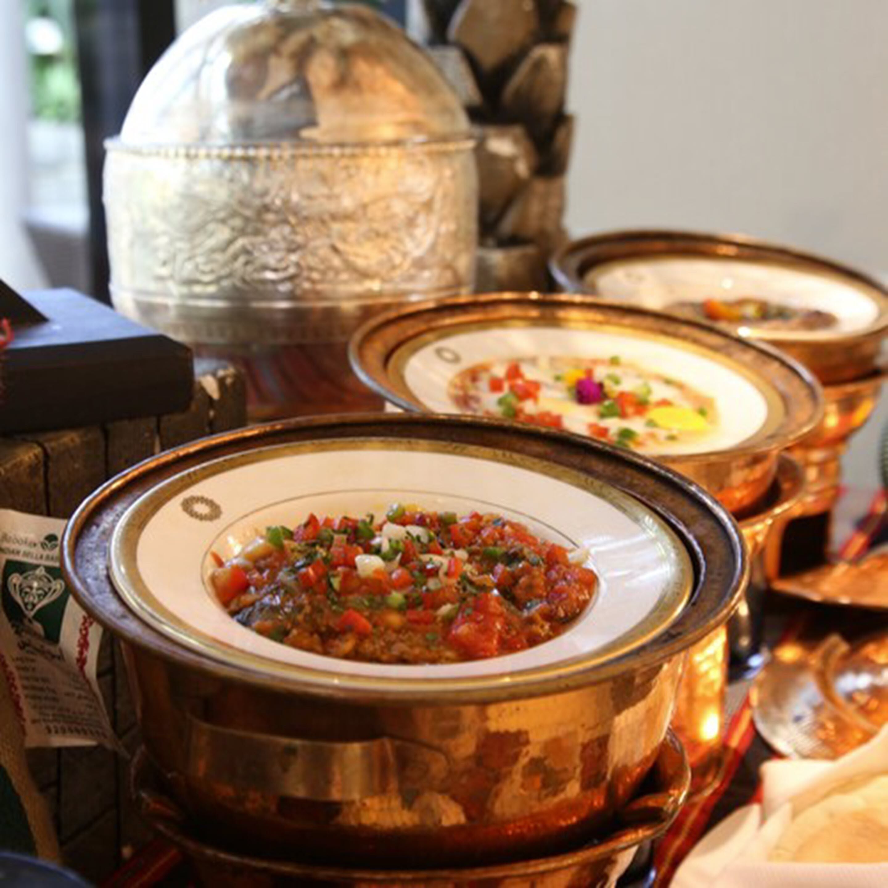 A table with several dishes in ornate metal bowls, suggesting a restaurant setting.