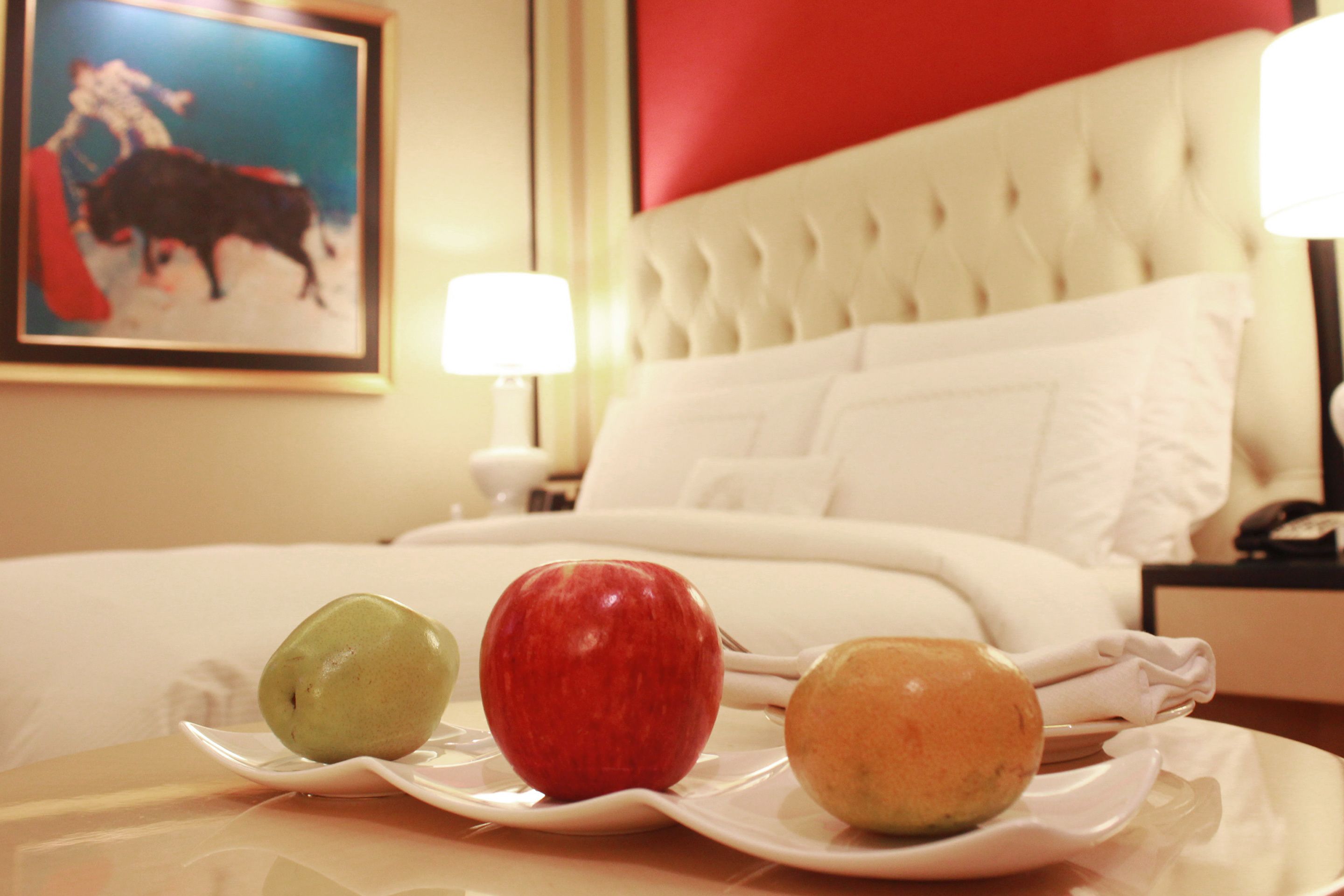 Een hotelkamer met een bed, een nachtkastje en een bord met drie appels op het nachtkastje.