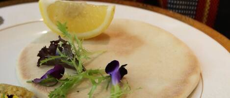 Une assiette contenant une galette, un quartier de citron, quelques feuilles de salade et un petit morceau de nourriture.