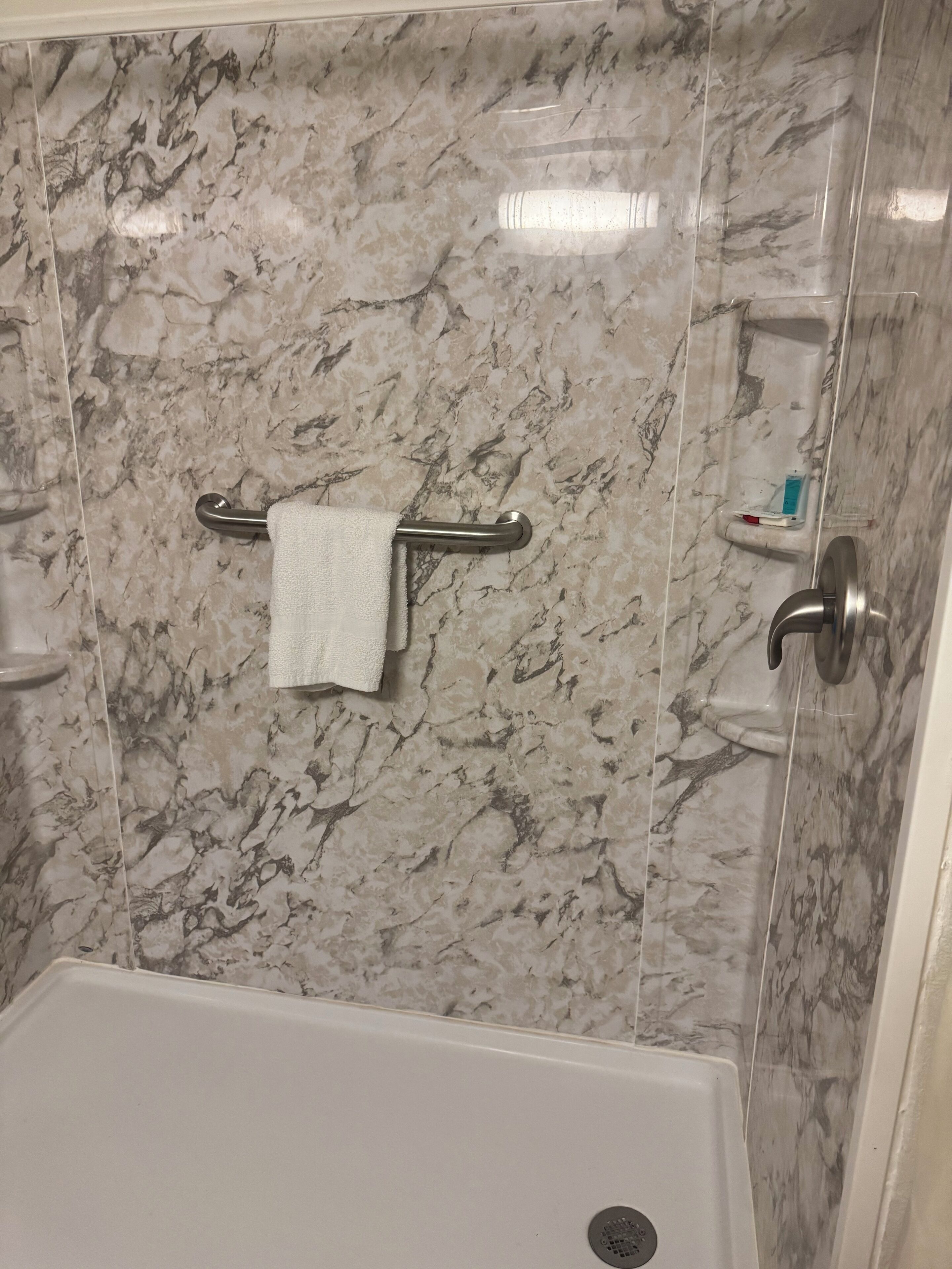 Une salle de bain avec un mur en marbre, un porte-serviettes, un distributeur de savon et un panneau de commande de la douche.