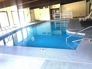 An indoor swimming pool with clear lanes, a lifeguard chair, and a poolside area with a white fence.