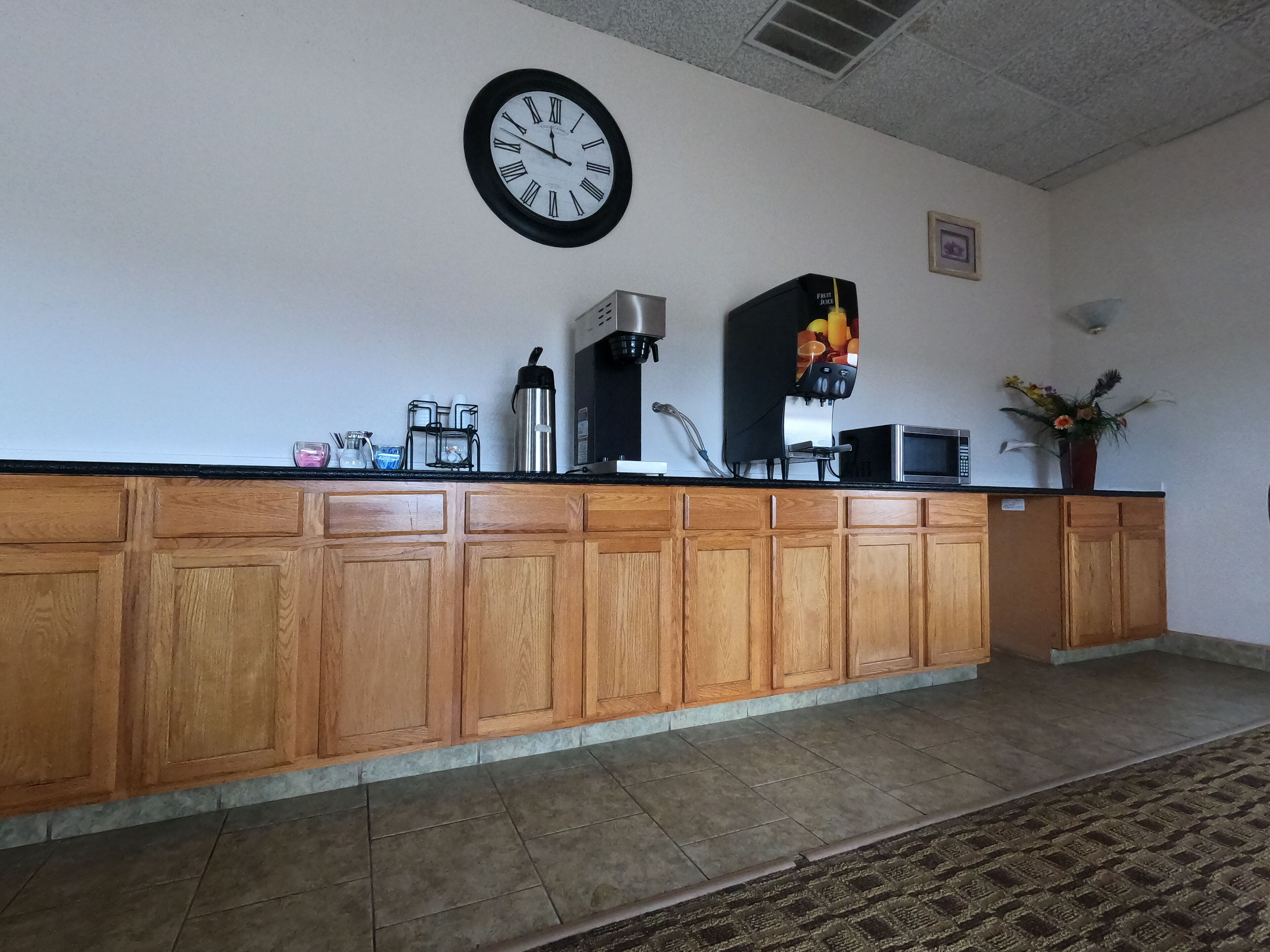 A kitchen area with wooden cabinets, a coffee machine, a microwave, and a clock on the wall.