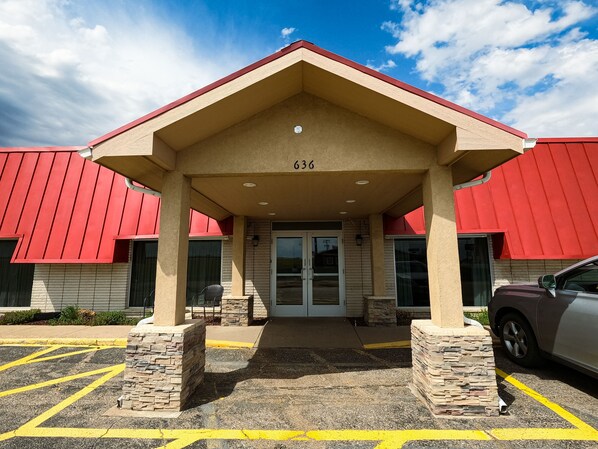 A building with a red roof and beige walls, numbered 636, featuring a covered entrance and a parking area.