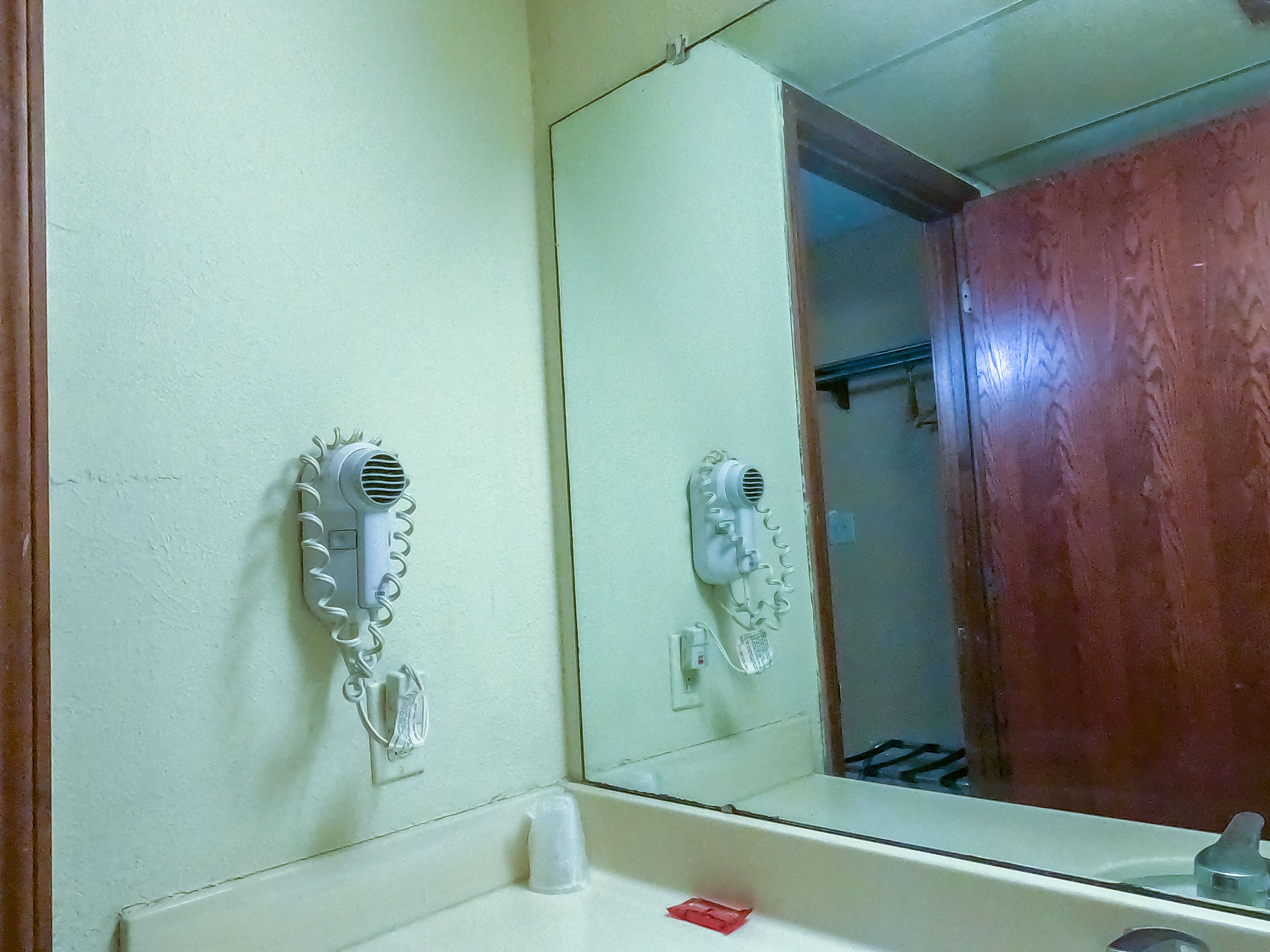 Une salle de bain avec un miroir, deux sèche-cheveux fixés au mur et un lavabo.