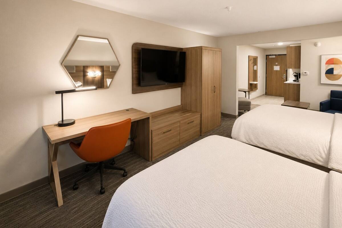 A hotel room with a desk, chair, TV, wardrobe, and two beds.