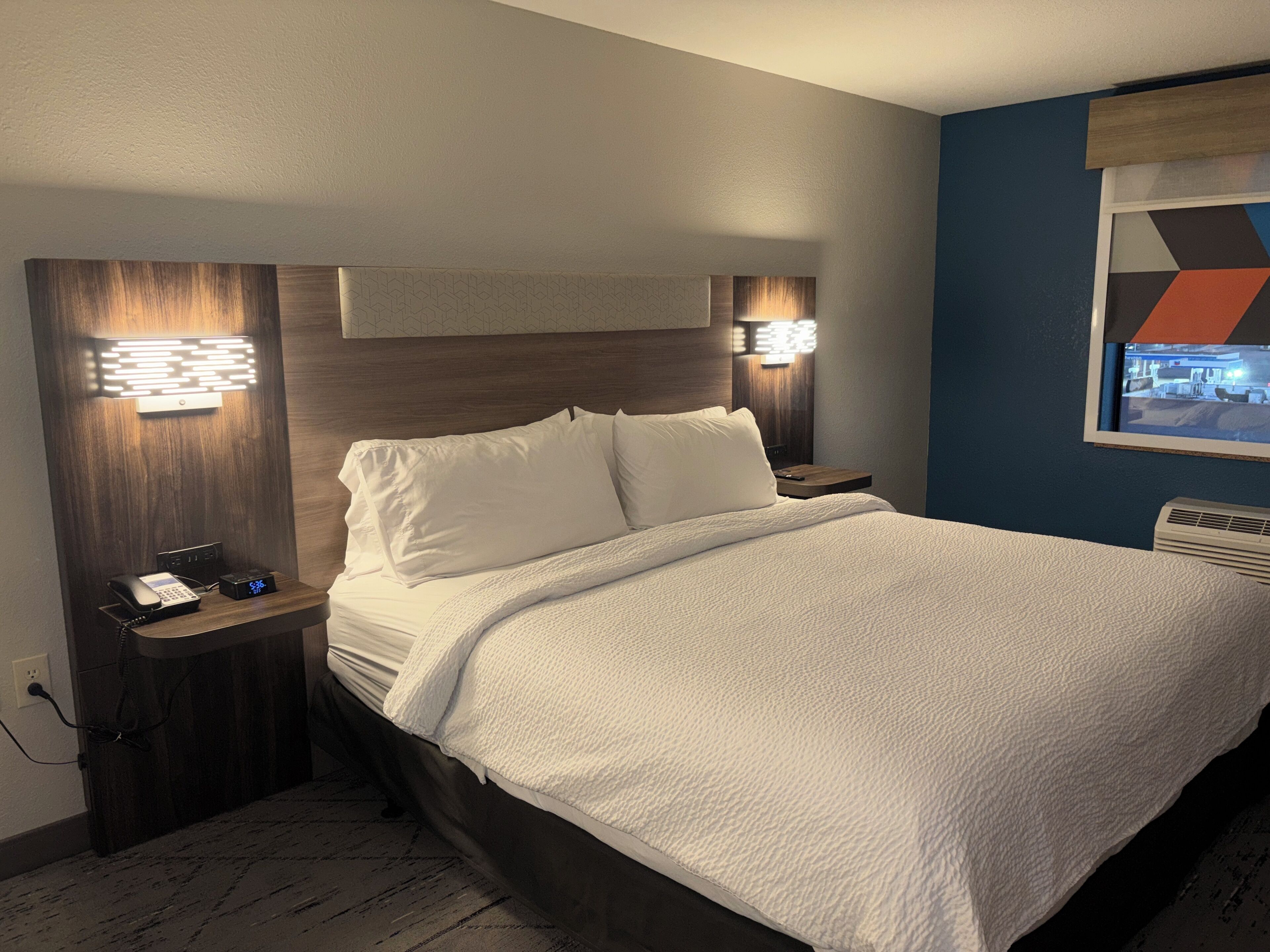 Habitación de hotel con una cama bien hecha, lámparas de noche, un teléfono y un televisor montado en la pared.
