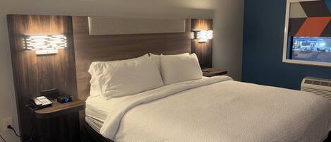 Habitación de hotel con una cama bien hecha, lámparas de noche, un teléfono y un televisor montado en la pared.