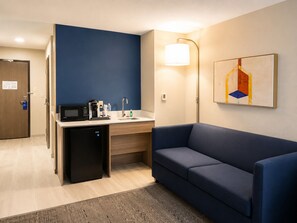 A compact hotel room with a kitchenette, a sofa, a painting on the wall, and a door. - Holiday Inn Express Hotel & Suites Truth or Consequences by IHG (Truth or Consequences)