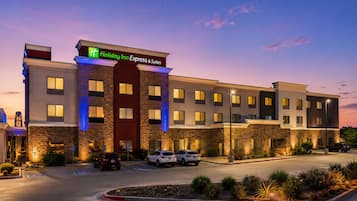 A Holiday Inn Express & Suites hotel with a modern design, featuring a stone facade, multiple parking spaces, and a landscaped entrance area.
