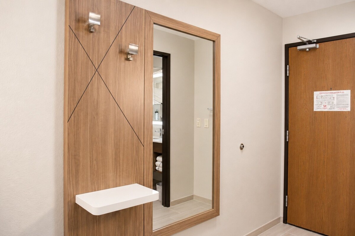 A room with a wooden wardrobe, a mirror, a white shelf, and a door with an emergency evacuation plan.