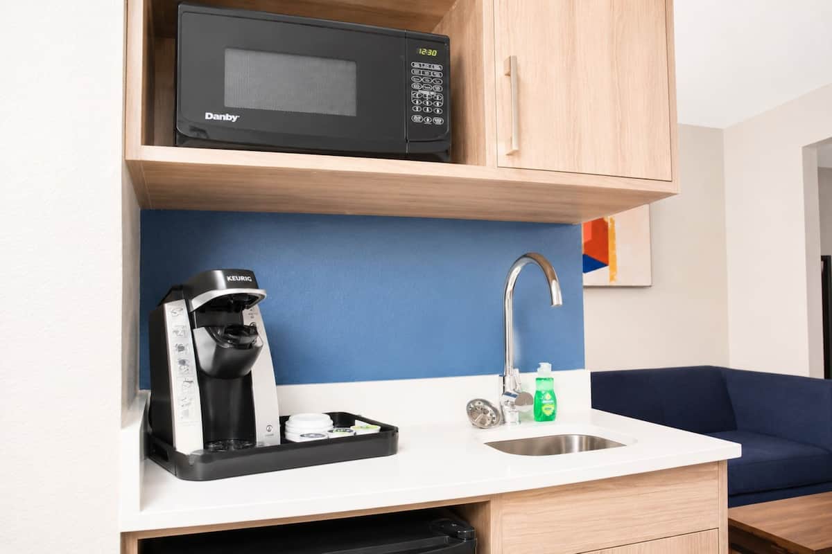 A compact kitchenette with a microwave, coffee maker, sink, and a blue wall.