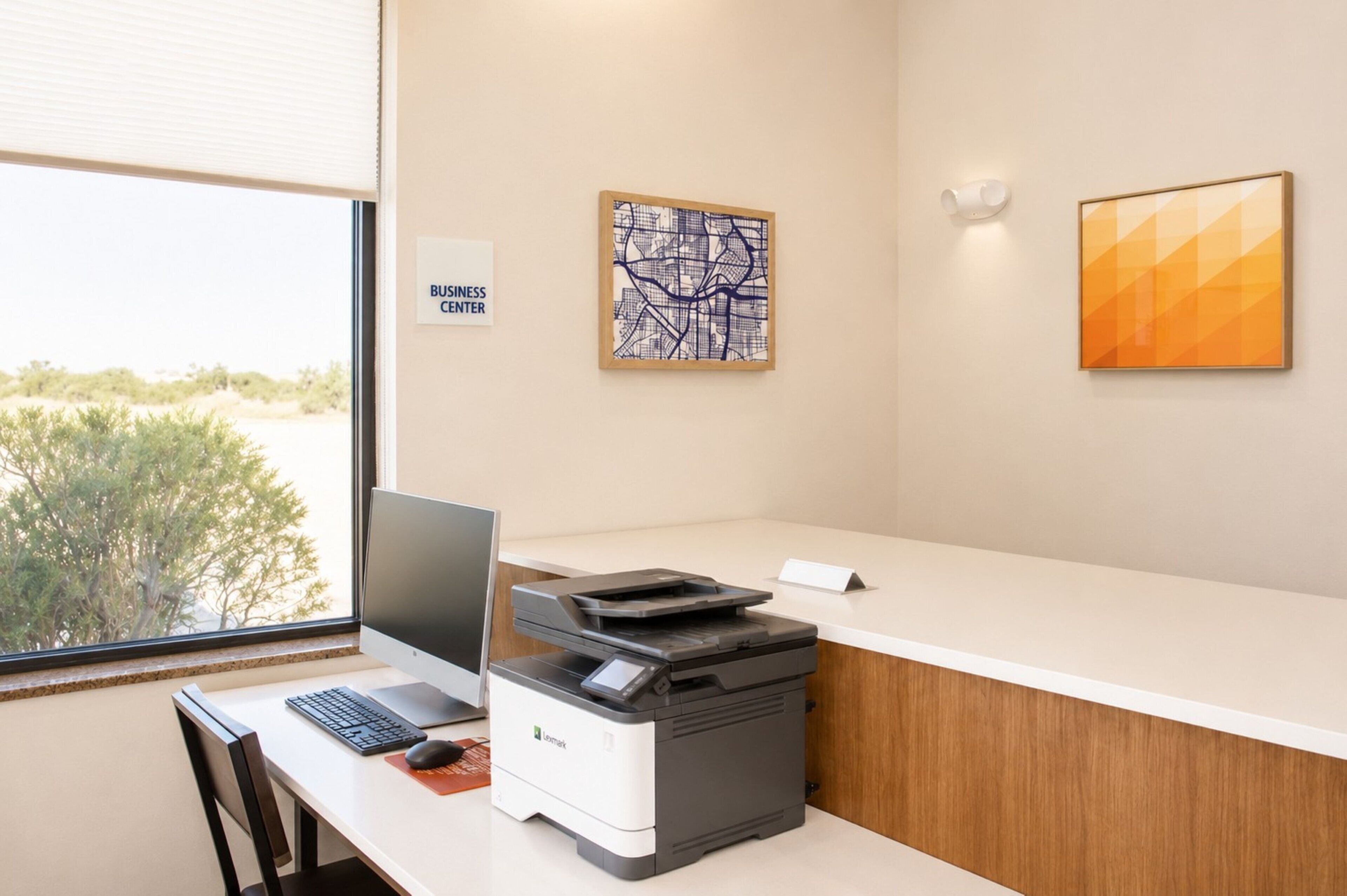 A business center with a desktop computer, printer, and a view of the outdoors.
