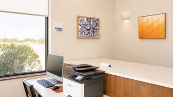 A business center with a desktop computer, printer, and a view of the outdoors.