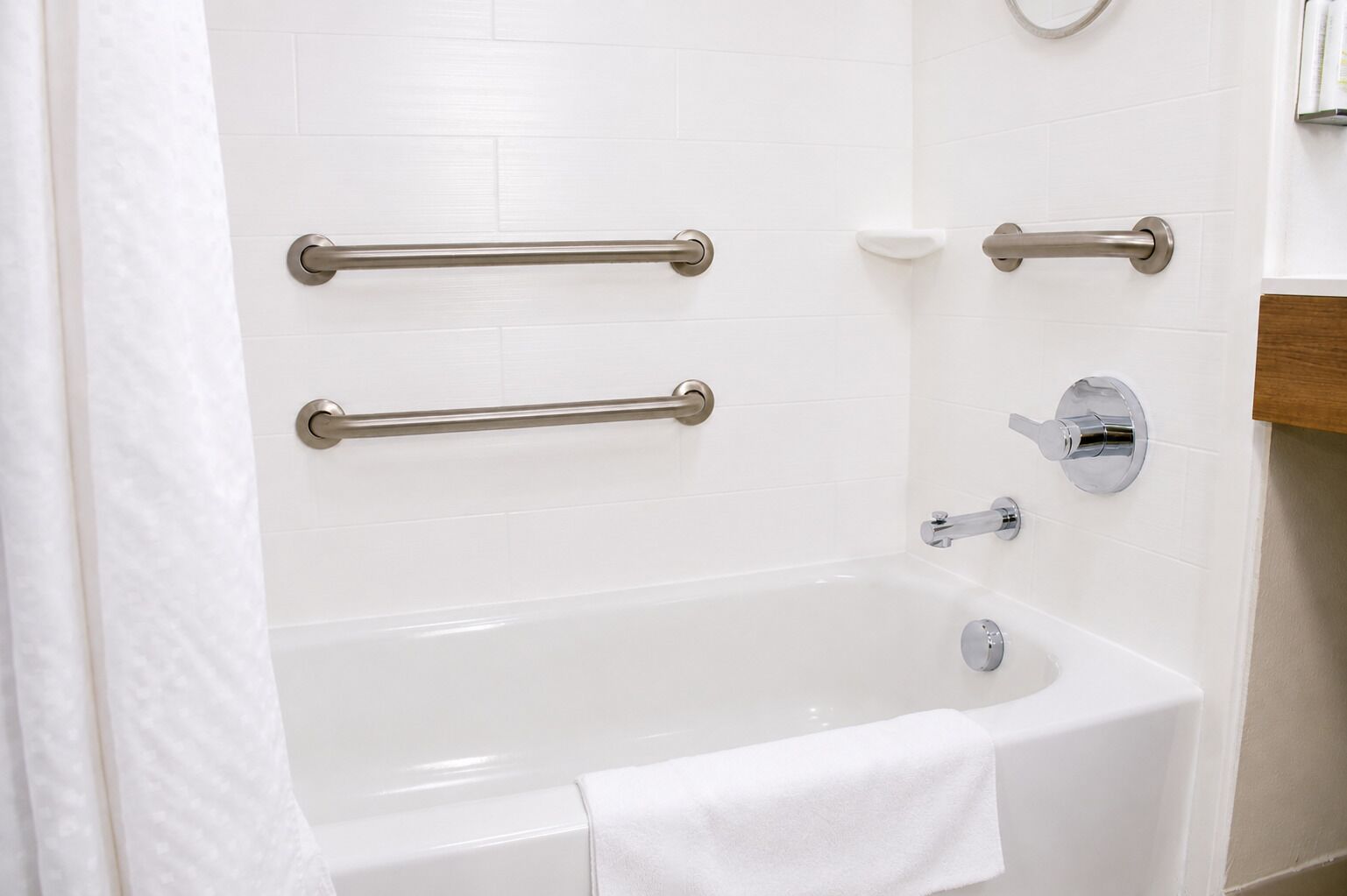 Une salle de bain avec une baignoire blanche, deux barres d’appui, un porte-savon et un porte-serviettes.