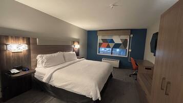Habitación de hotel con cama, mesita de noche con teléfono, escritorio con silla, ventana con vistas y aire acondicionado instalado en la pared.