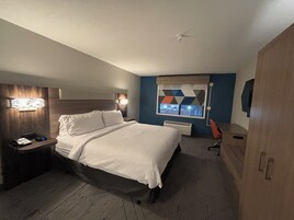 Habitación de hotel con cama, mesita de noche con teléfono, escritorio con silla, ventana con vistas y aire acondicionado instalado en la pared.