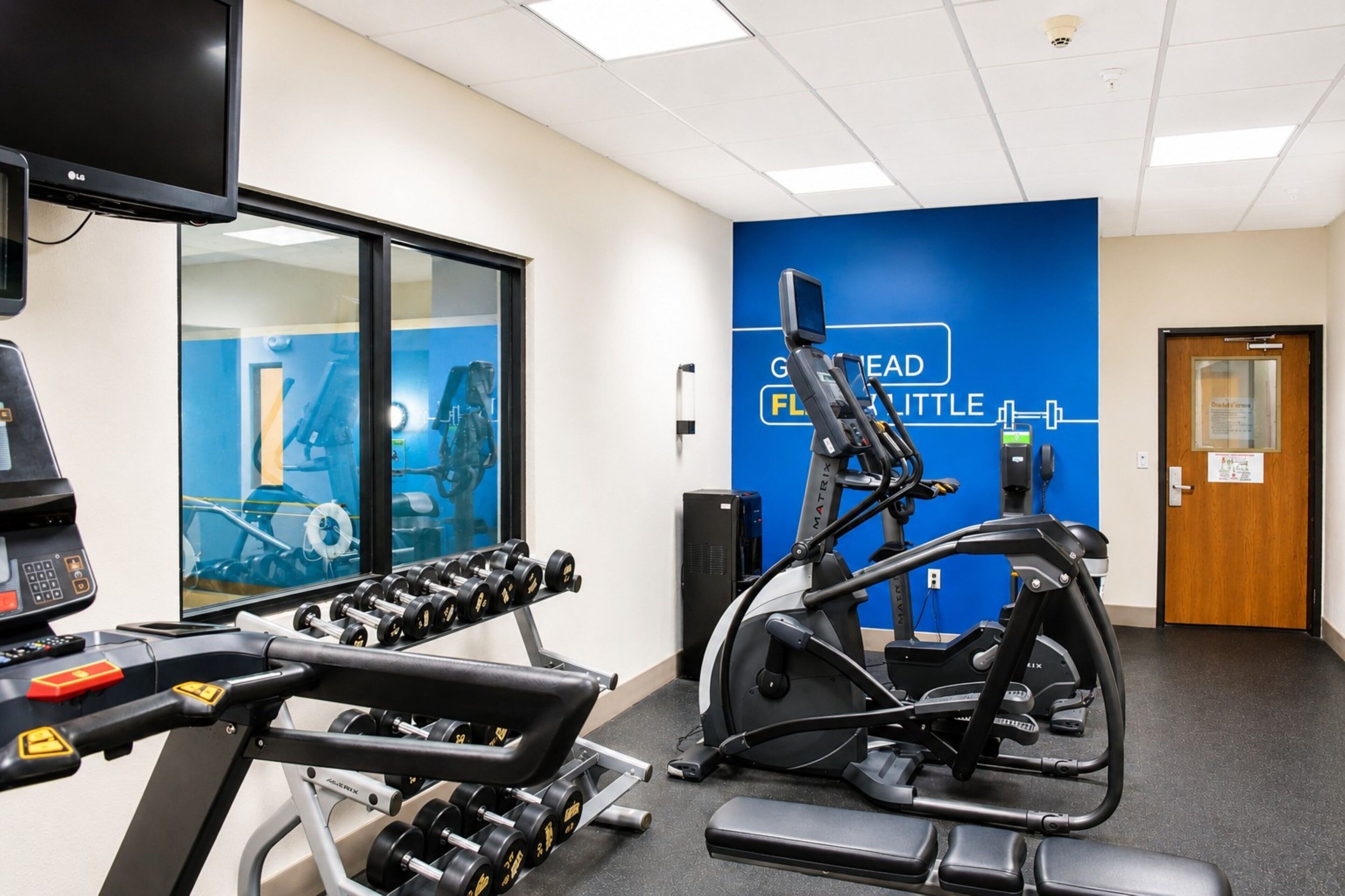 A gym with exercise equipment, a television, and a blue wall with text.