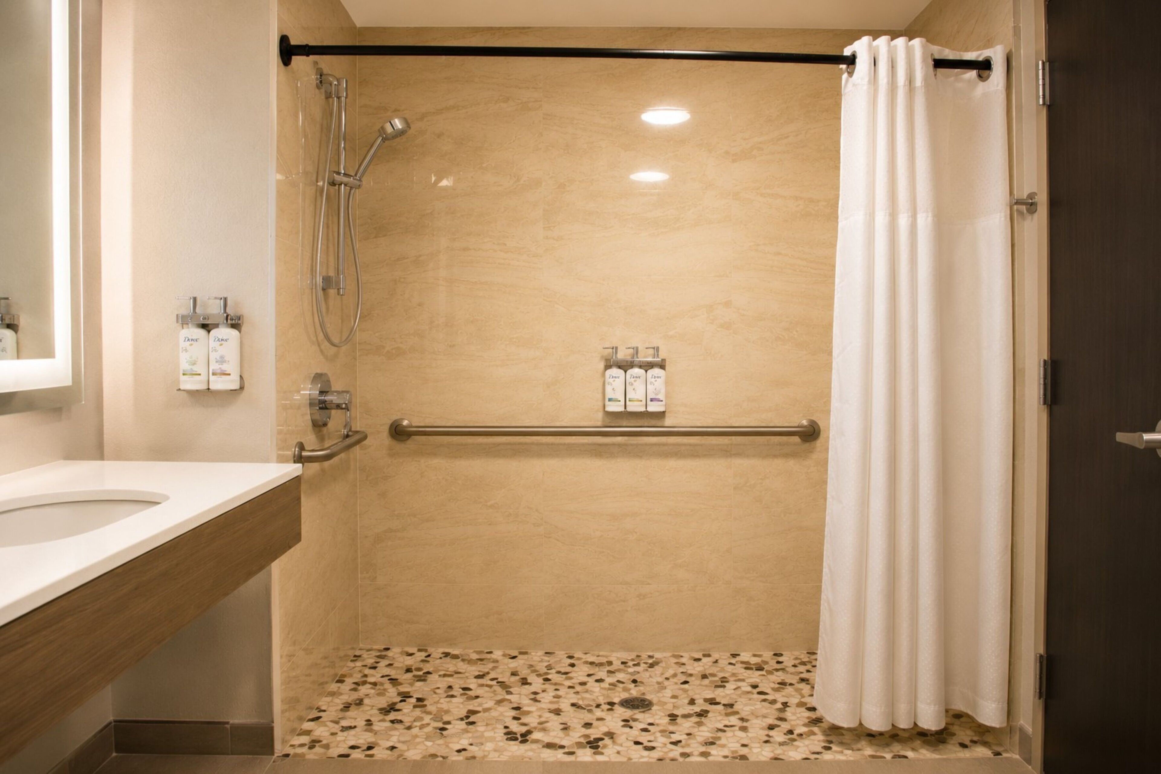 A bathroom with a shower, a handrail, and a tiled floor.