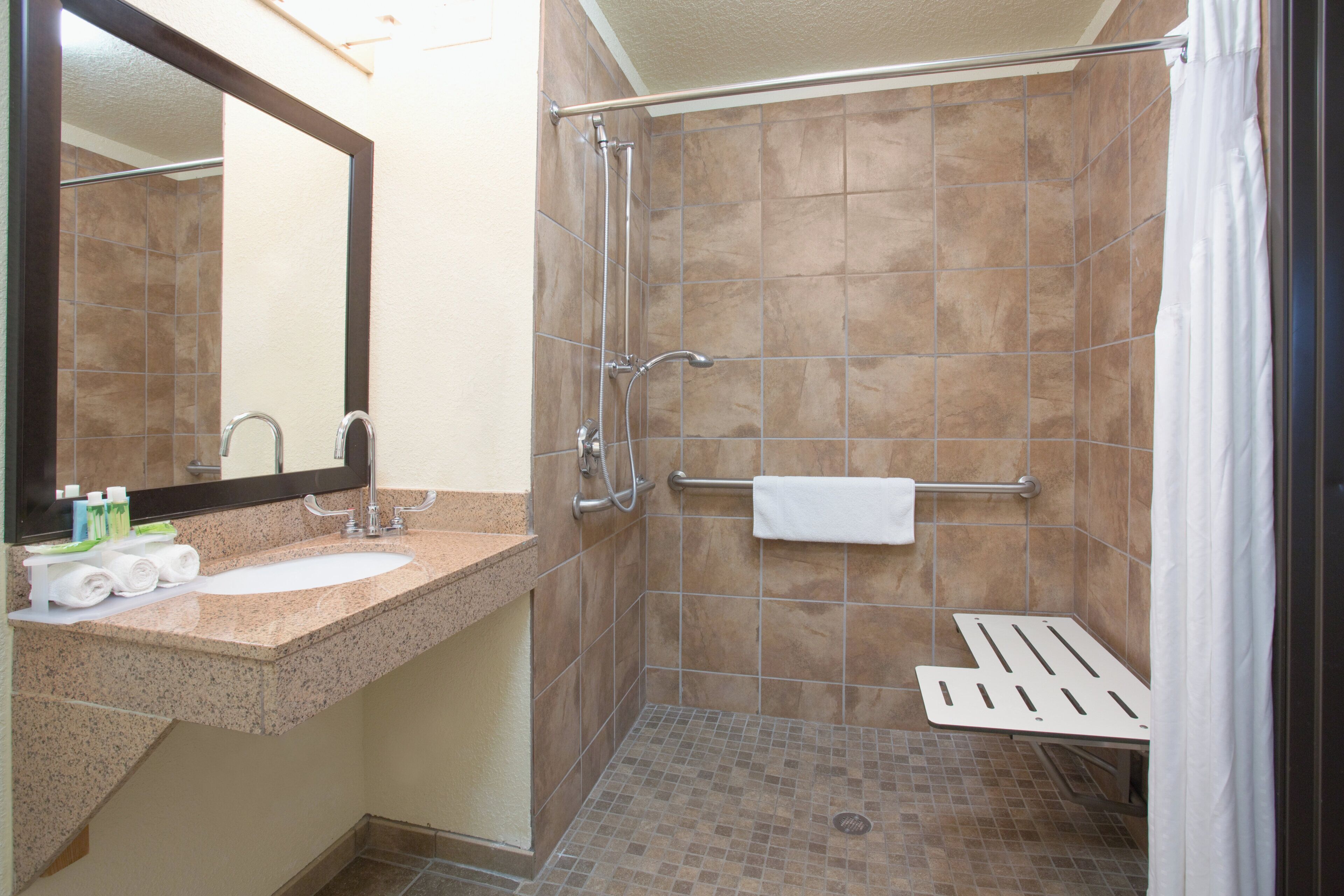 A bathroom with a sink, mirror, towel rack, shower, and a white towel.