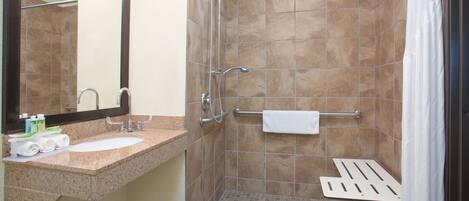 A bathroom with a sink, mirror, towel rack, shower, and a white towel.