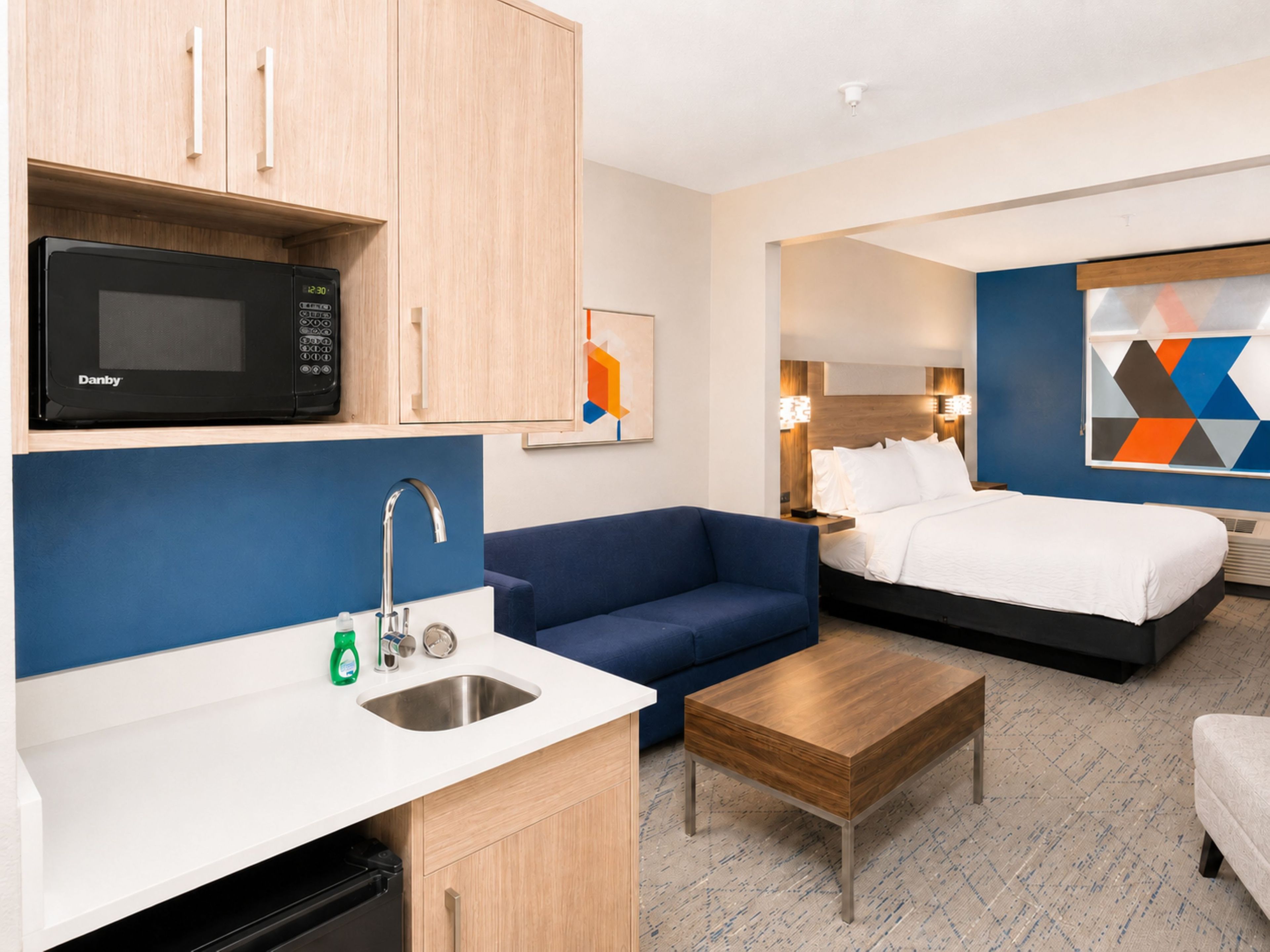 Hotellihuone, jossa on pieni keittiö, sänky, sohva ja sohvapöytä.
