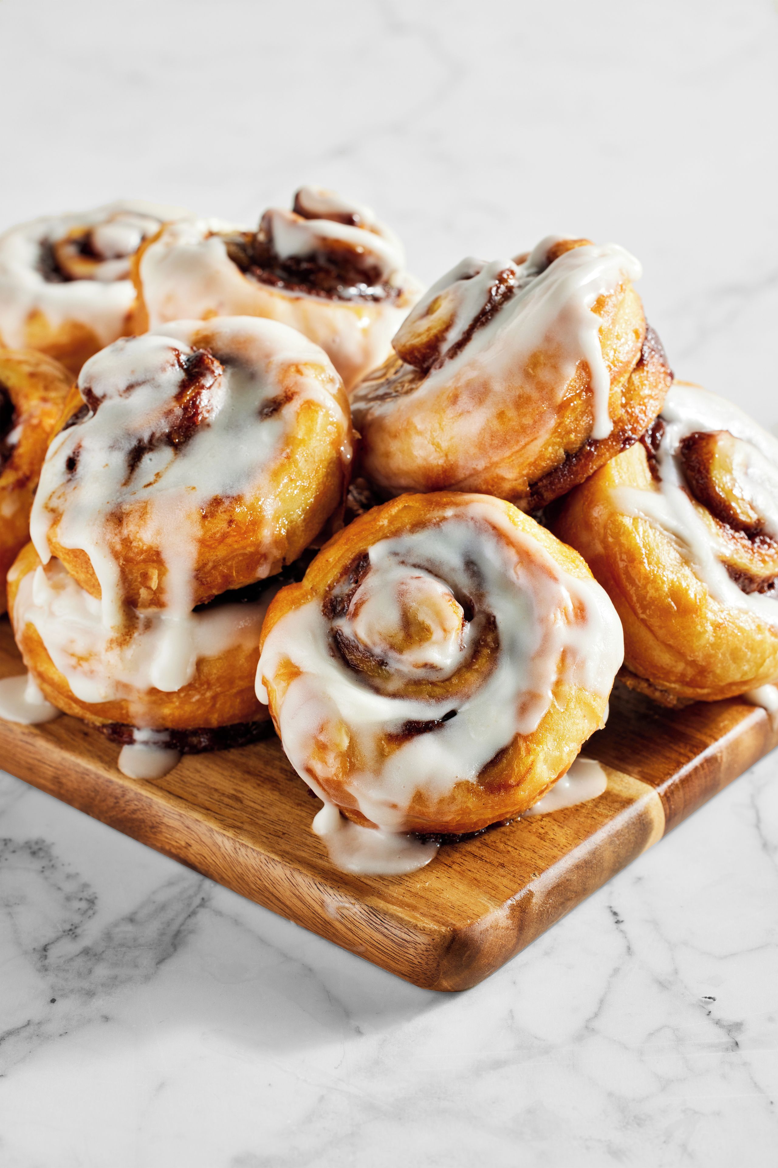 A tray of cinnamon rolls with icing on a wooden board.