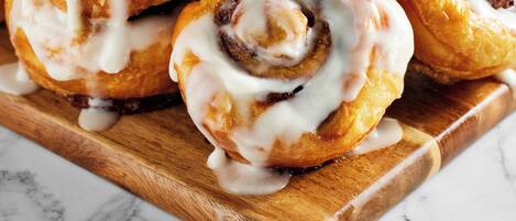 A tray of cinnamon rolls with icing on a wooden board.