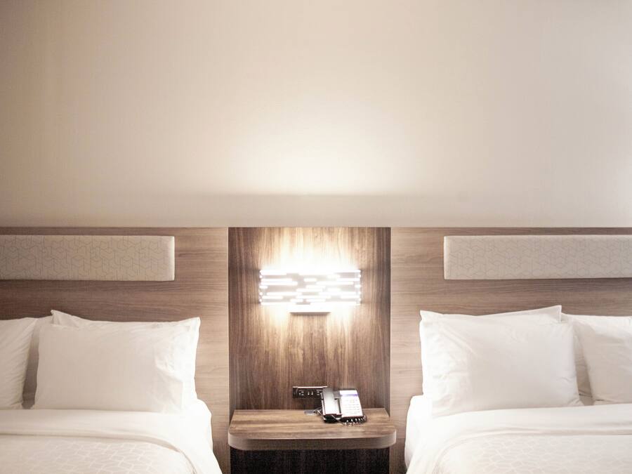 Una habitación de hotel con dos camas, una mesita de noche con teléfono y una lámpara fijada a la pared.