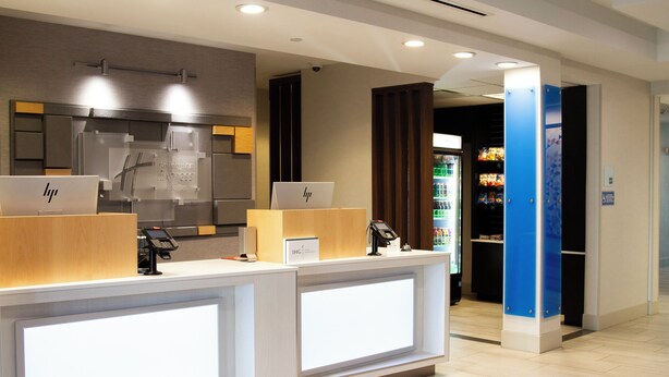 A hotel reception area with two reception desks, a digital display, and a vending machine in the background. - Holiday Inn Express and Suites Overland Park by IHG (Overland Park)