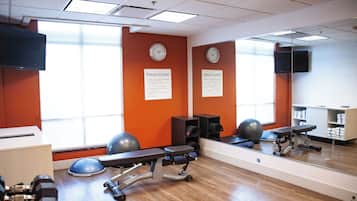 Un gimnasio con equipo de ejercicio, un espejo grande y relojes en la pared.