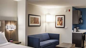 Quarto de hotel com cama, sofá azul, mesinha, escrivaninha, abajur e quadros nas paredes.