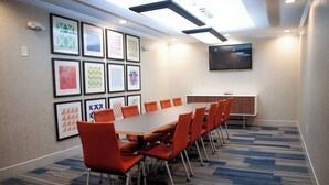 A conference room with a long table and orange chairs, framed artwork on the walls, and a flat-screen TV. - Holiday Inn Express and Suites Overland Park by IHG (Overland Park)