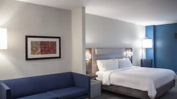 A hotel room with a bed, a blue sofa, a framed picture on the wall, and a bedside table with a lamp.