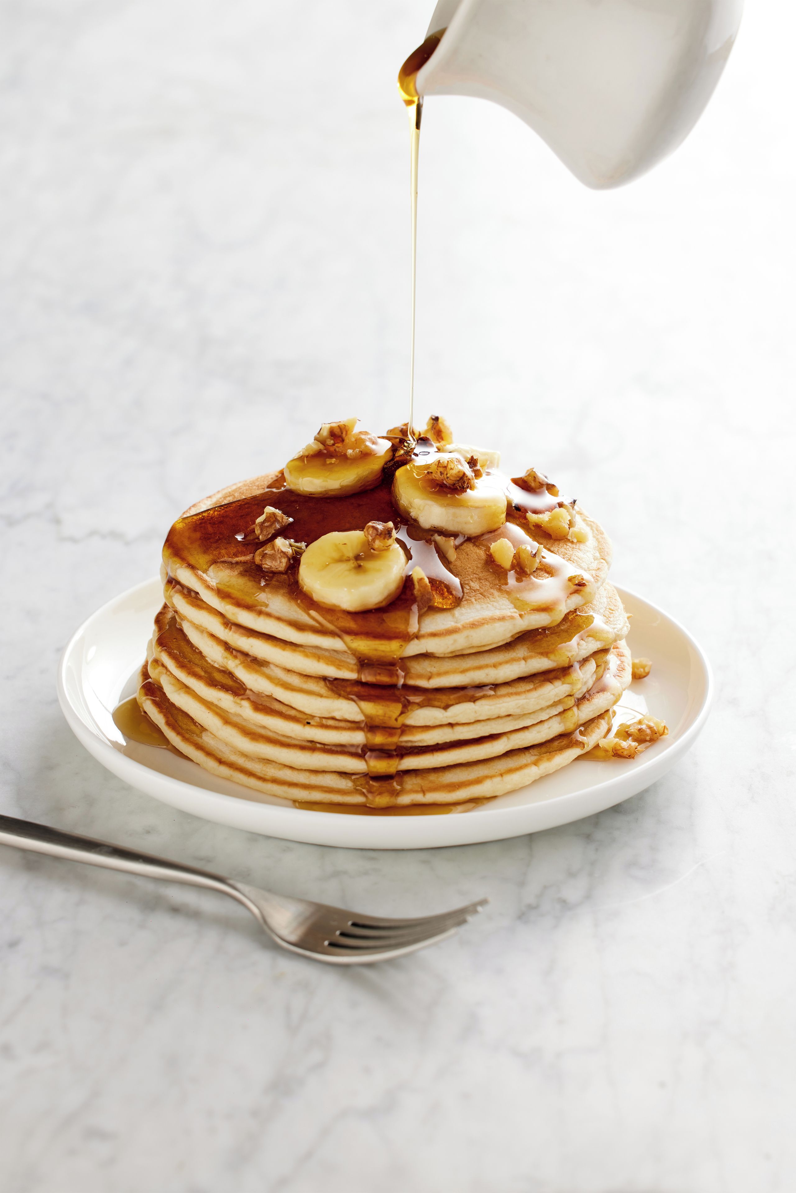 A stack of pancakes with syrup and banana slices on a white plate.